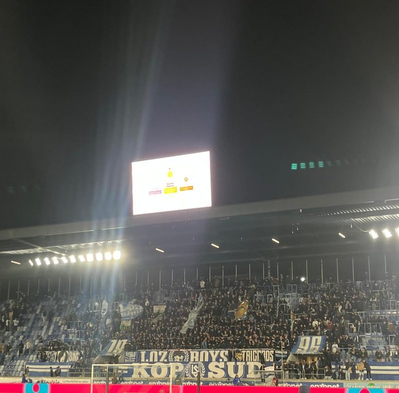 Le virage Kop Sud du stade de la Tuilière, les supporters du Lausanne-Sport un soir de match, avec l'écran géant en fond.