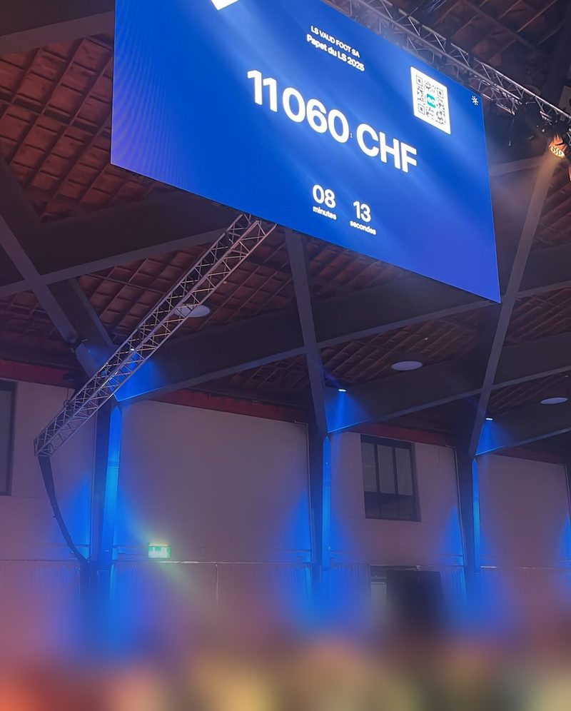Soirée de gala du LS — grand écran LED affichant le compteur Live Wall à 11 060 CHF au-dessus des tables ; les personnes au premier plan sont volontairement floutées.