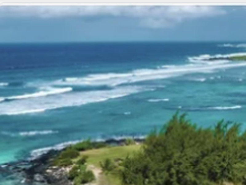 Île Maurice : lagon turquoise et vagues déferlant sur la barrière de corail, bordé d'une pointe verdoyante et de cocotiers.