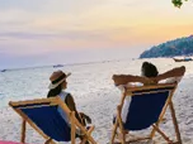 La Réunion : deux personnes en transats face à l'océan au coucher du soleil, sur une plage de sable fin, ciel rose et doré.