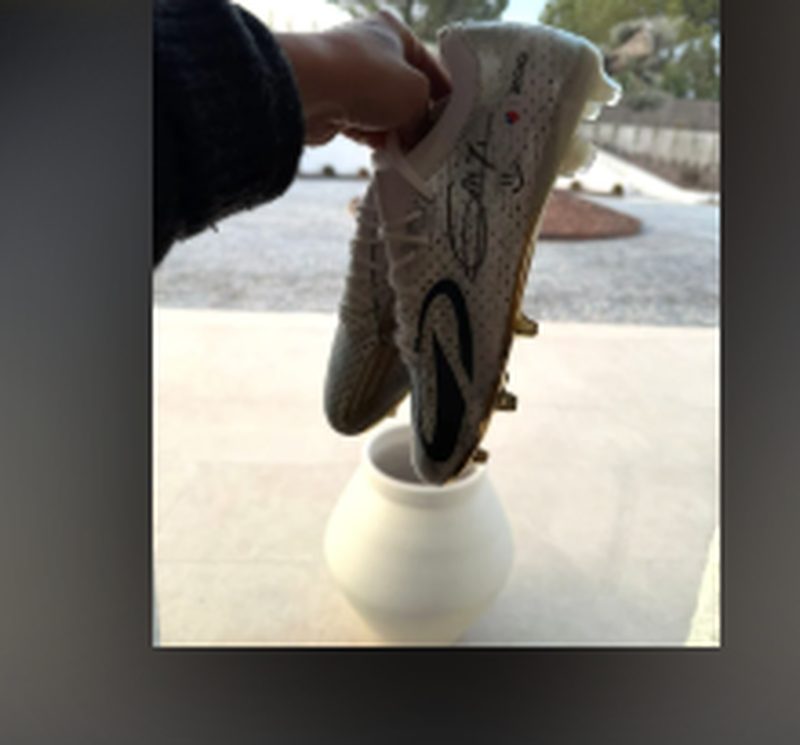 Paire de crampons de football en édition limitée dédicacée par Antoine Griezmann, présentée tenue à la main devant un stade.